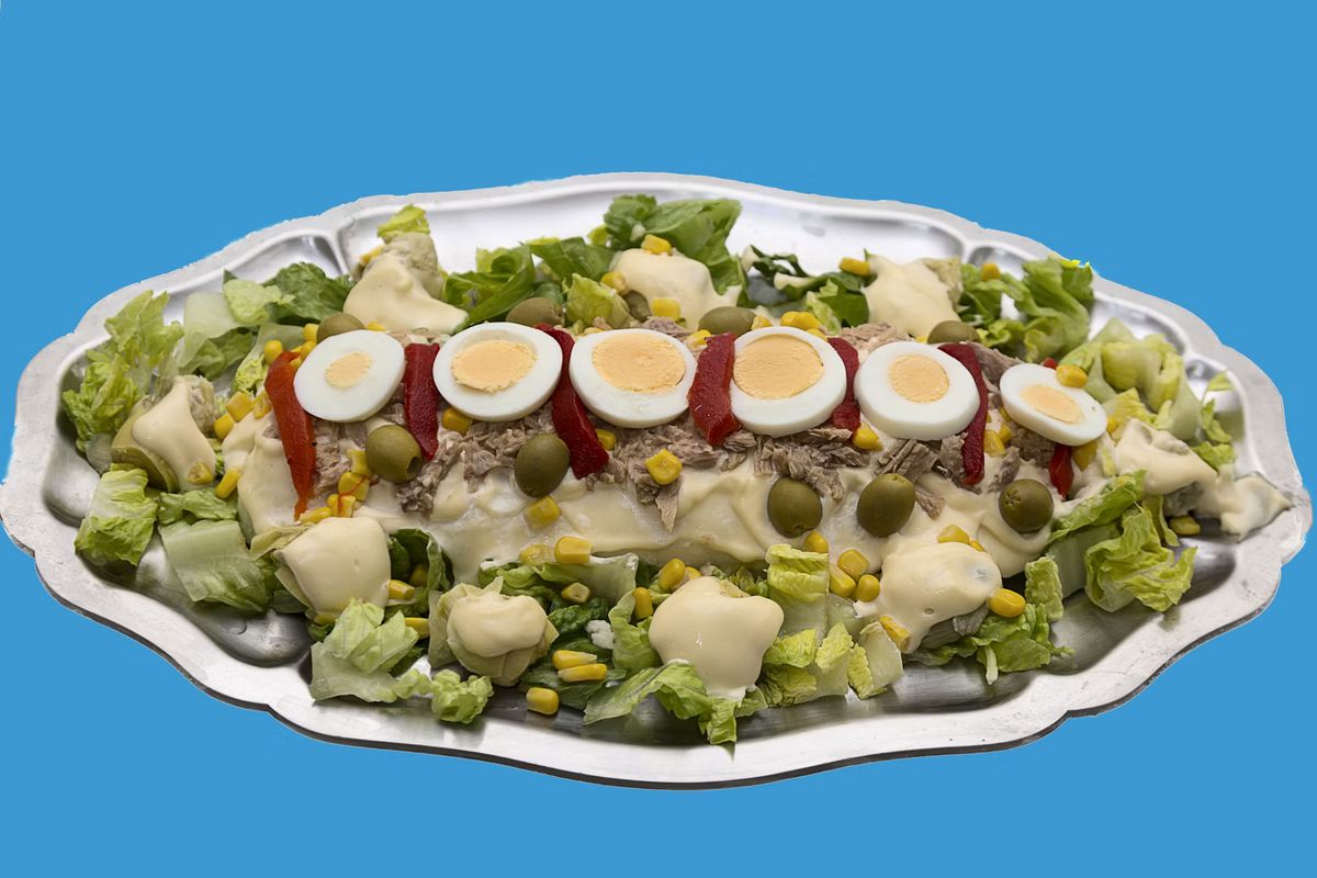 Ensaladilla rusa auf einer Silberplatte, mit Eierscheiben, Paprikastreifen, Oliven, Thunfisch und Mais auf Salatblättern